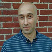 man in striped polo leaning against brick wall