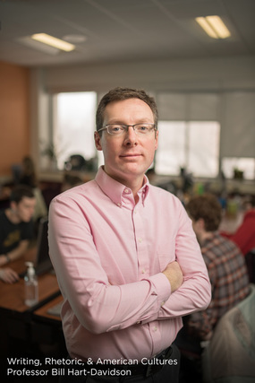 man in pink button down standing up in classroom