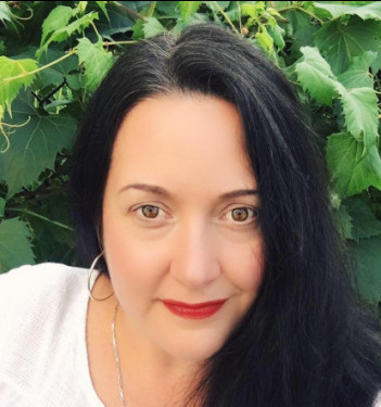 woman in foliage looking into camera - she has dark hair and bright red lipstick