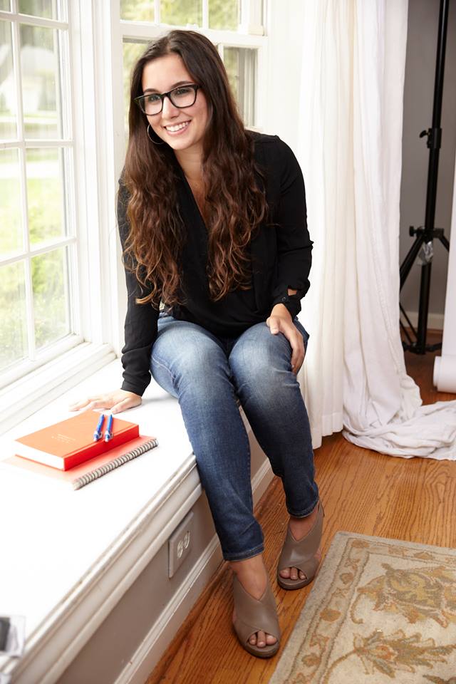 portrait of a girl with brown hair and glasses sitting on white window sill