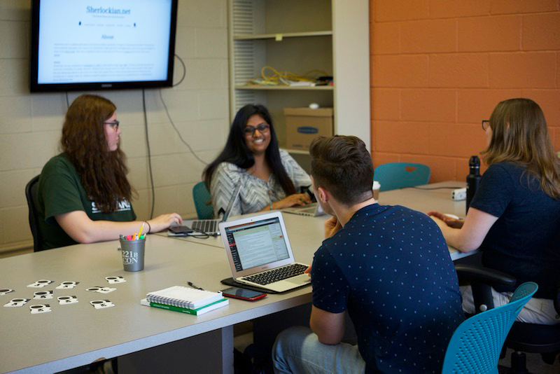 group of students working together on laptop with a screen in the background