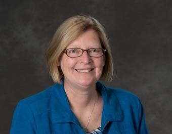 woman with short blonde hair wearing glasses and a blue top