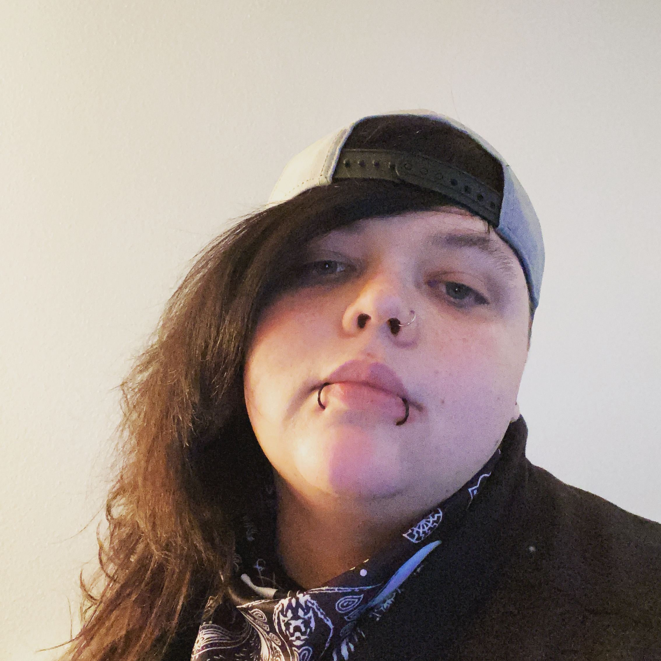 A person with lip piercings wearing a ball cap backwards