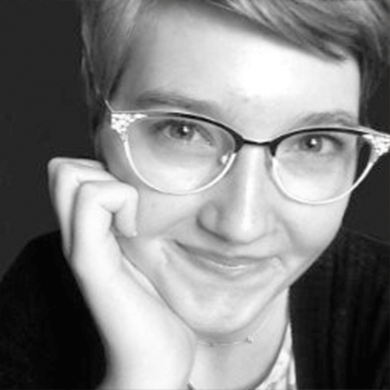 Close-up of a person with short hair and glasses resting their hand against their cheek