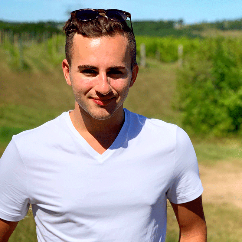 A young man in a white tee shirt standing in a green field on a sunny day