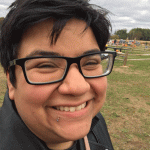 Headshot of a person with short dark hair and glasses with black frames