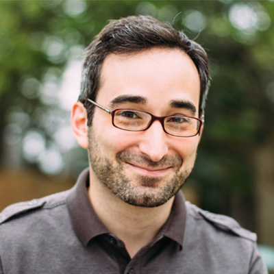 Man with short brown hair wearing glasses and a brown dress shirt.