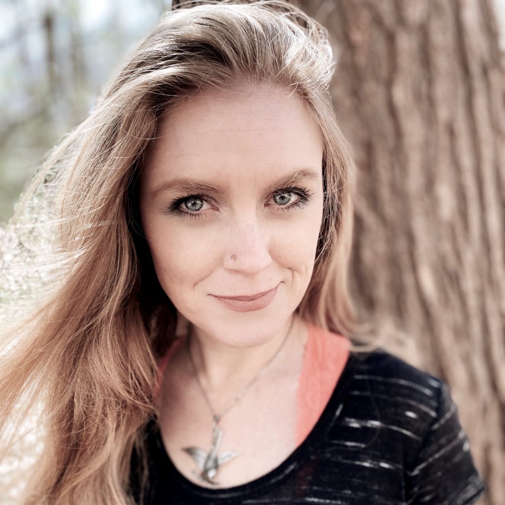 Woman standing in front of a tree, wearing a black shirt and smiling.