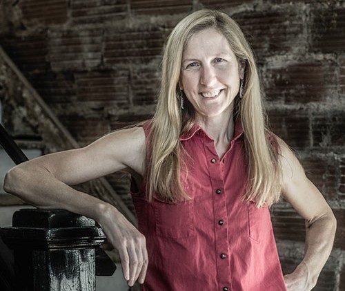 Photo of a woman with long strawberry blonde hair and a sleeveless button-up top. 