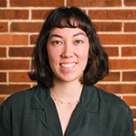 photograph of a smiling person standing in front of a brick wall