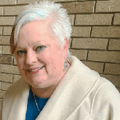 woman with gray hair smiling and standing in front of a brick wall