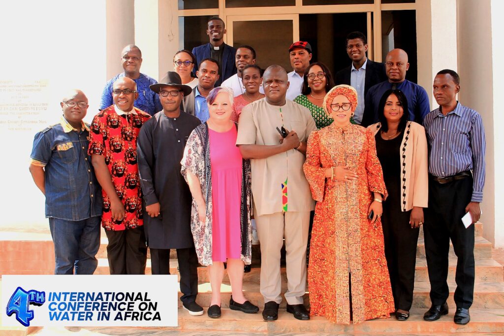 A group of approximately 20 conference attendees poses on the steps outside a building during the 4th International Conference on Water in Africa. Participants are dressed in a variety of professional and traditional attire, standing in rows and smiling toward the camera. A conference logo is visible in the bottom left corner of the image.