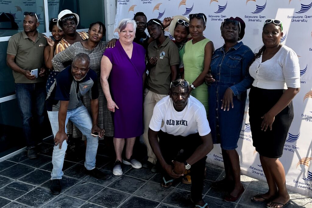 A group photo with 13 people posing to have their photo taken in front of a step and repeat screen that has a logo and says "Botswana Ocean University." 