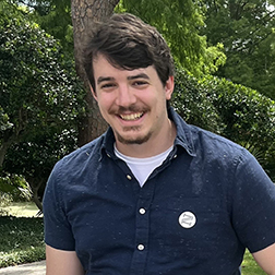 smiling man wearing blue shirt standing in front of trees