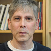man with gray hair in front of a bookshelf