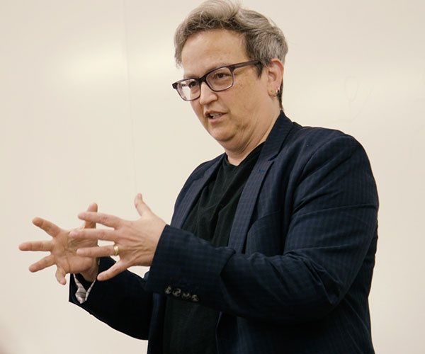 a person wearing glasses giving a talk and wearing a navy blue blazor