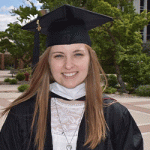 A young woman with long hair wearing a black graduation cap and gown over a lacy white top