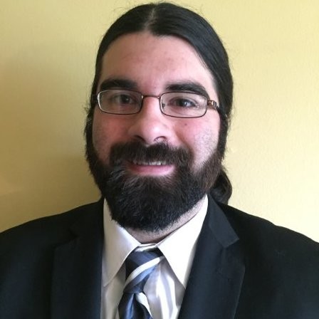 Image of a bearded man wearing a suit and tie with his hair in a ponytail