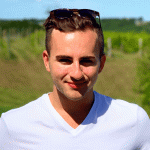 A young man in a white tee shirt standing in a green field on a sunny day