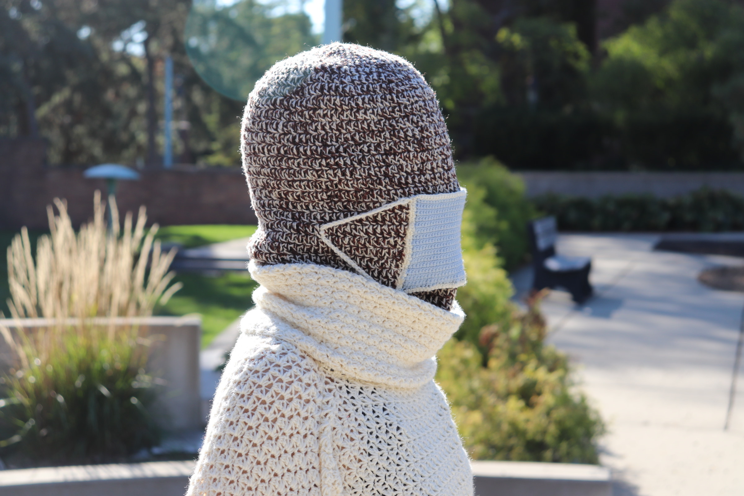 Zoomed in side view of person standing wearing the sweater covering their head and the white turtleneck and the disposable mask.