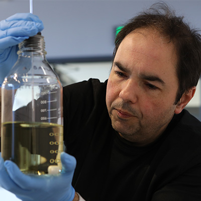 Man with brown hair holding a clear test tube with liquid in it.