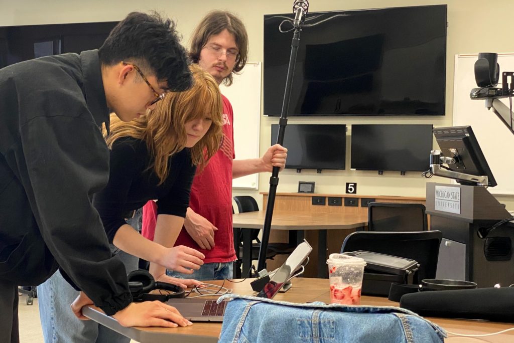 Three students gather around a computer to edit their radio drama.