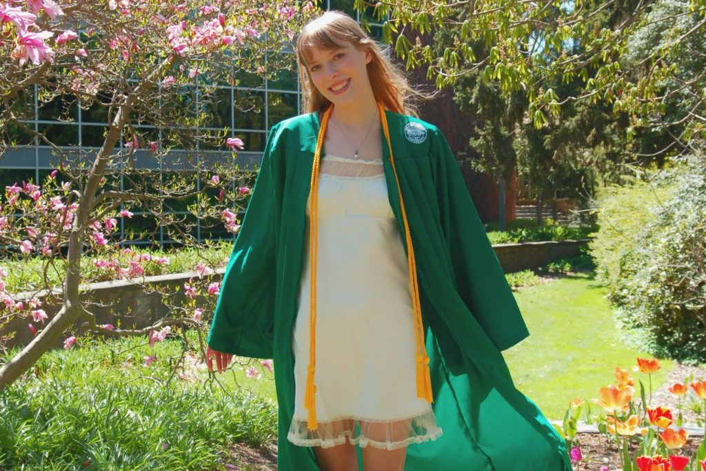 A picture of a woman in a green gown and white dress standing in a garden.