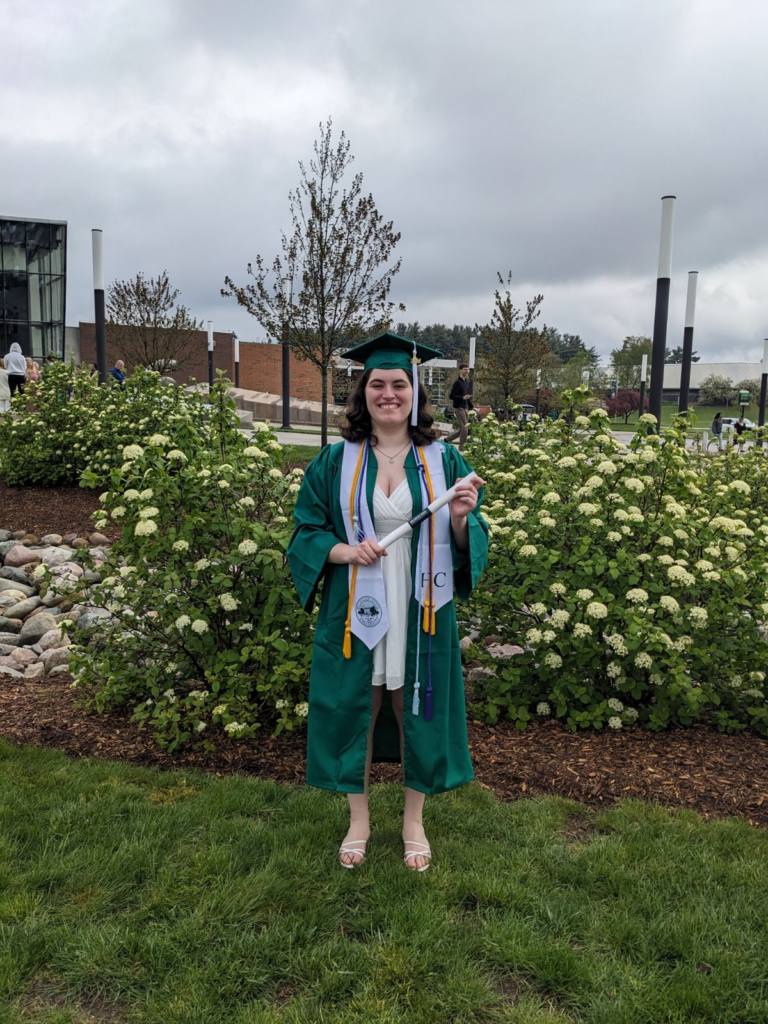 Kira Vander Molen stands in a white dress and green graduation cap and gown. 