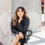 a woman with long dark hair wearing a black dress sitting on a stone bench